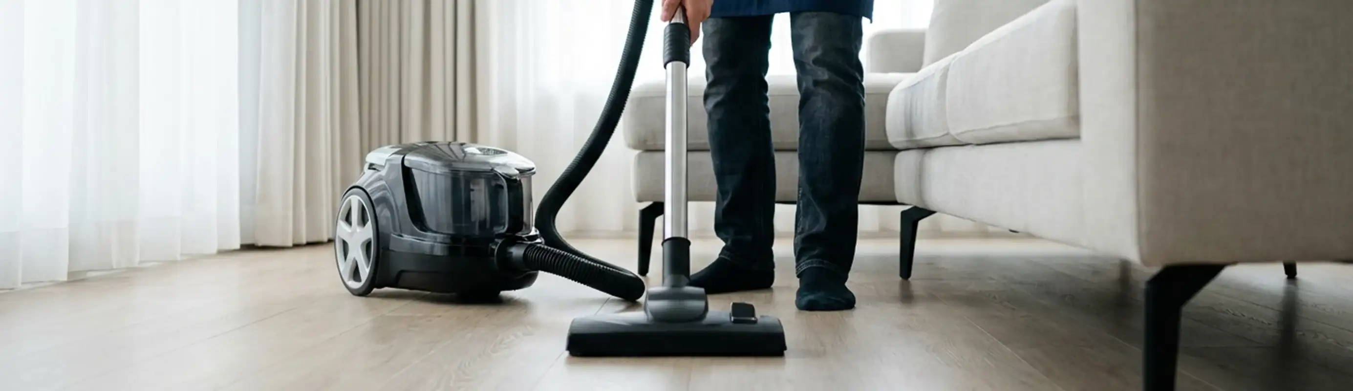 Professional house cleaner vacuuming a living room floor with a canister vacuum cleaner, Columbus, OH.
