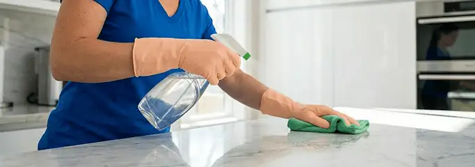 Maid service worker spraying and wiping a kitchen countertop with a microfiber cloth for sanitizing, Columbus, OH.