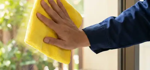 House cleaner wiping a glass window with a yellow microfiber cloth for streak-free cleaning, Columbus, OH.